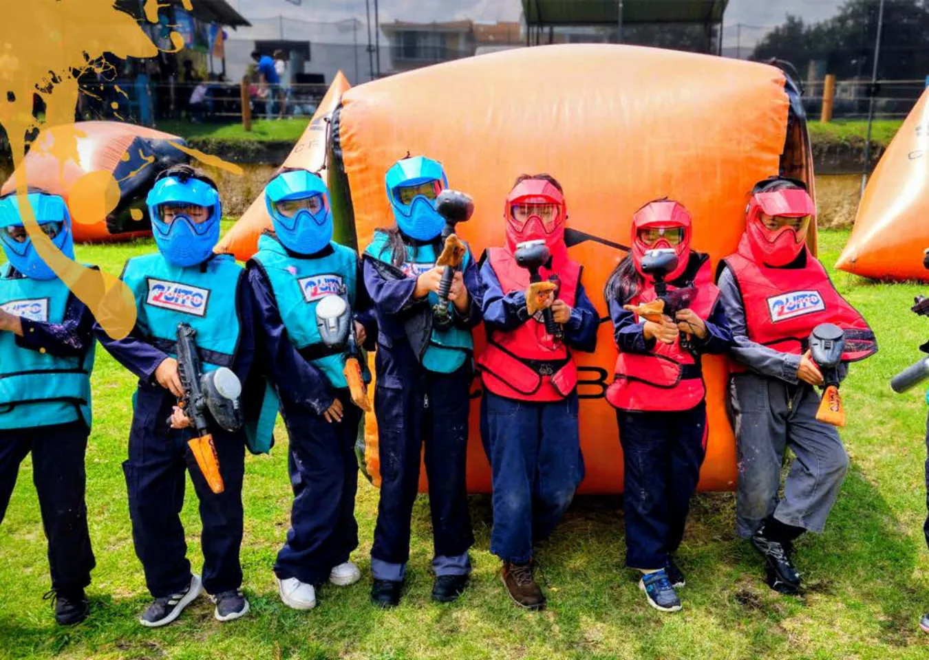 Niños con máscaras rojas y azules y marcadoras frente a un obstáculo inflable