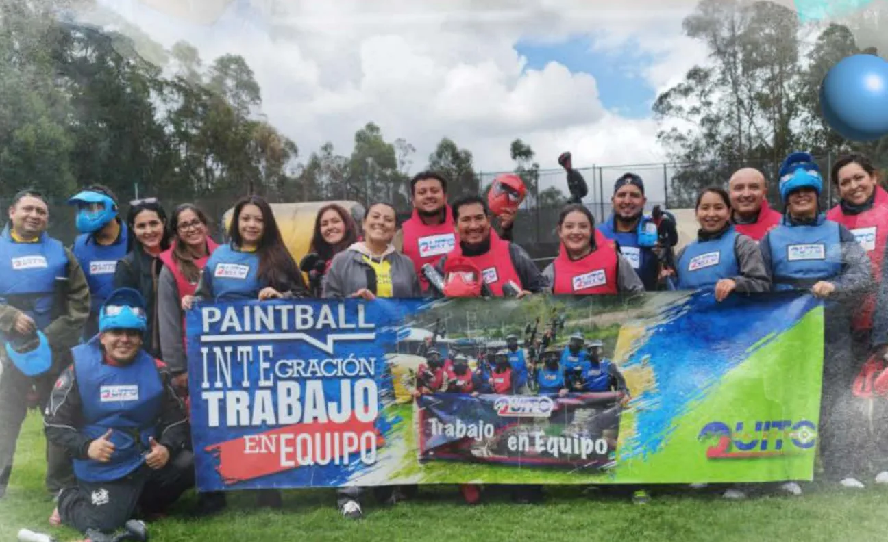 Grupo de una empresa con máscaras y chalecos sostiene la pancarta de Paintball Integración Trabajo en Equipo